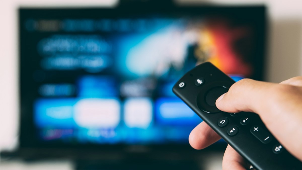 Hand pressing the navigation button on a streaming remote in front of a television